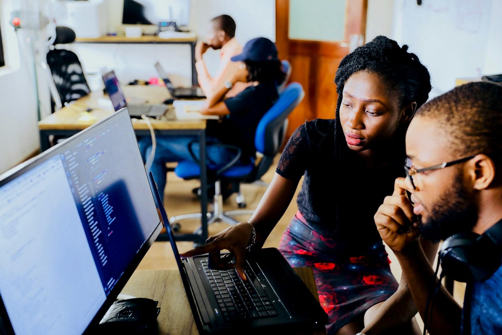 Two engineers reviewing code together on a laptop in an open-plan office.