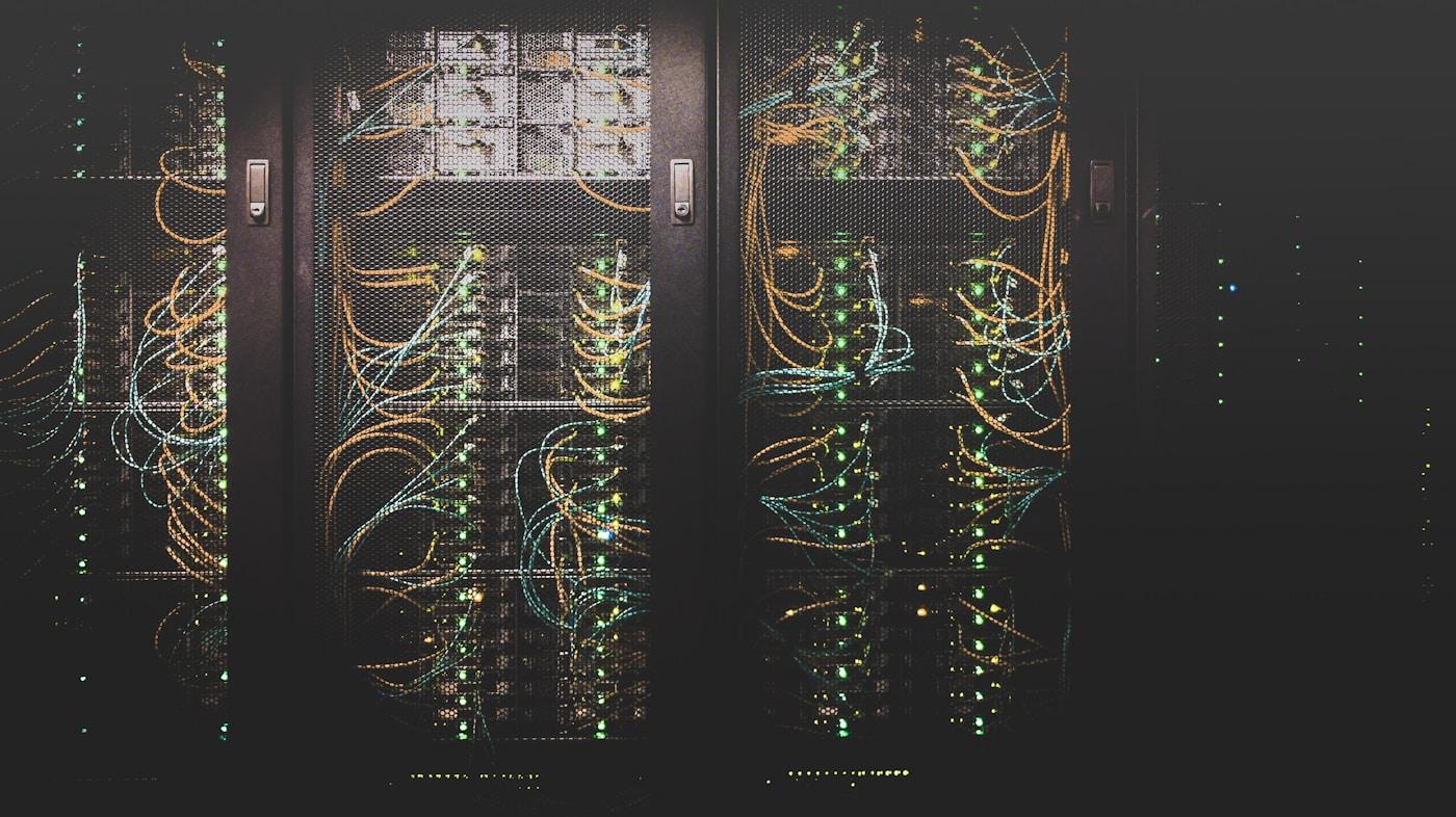 Server racks in a dark data centre, threaded with bundles of network cable.