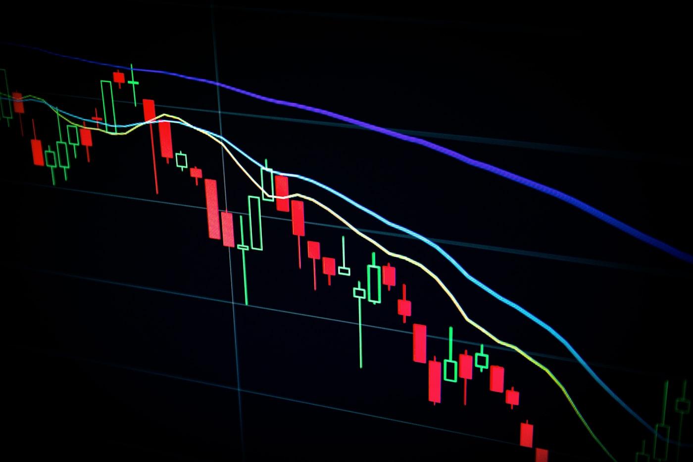 A trading chart of red and green candlesticks falling across a dark screen.