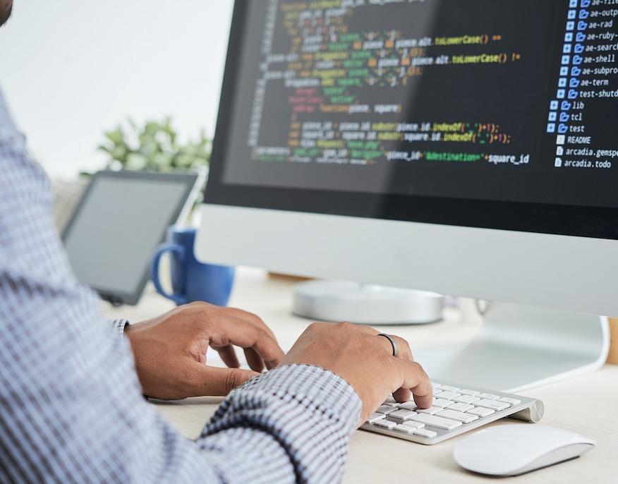 A developer typing at a desktop machine showing source code.